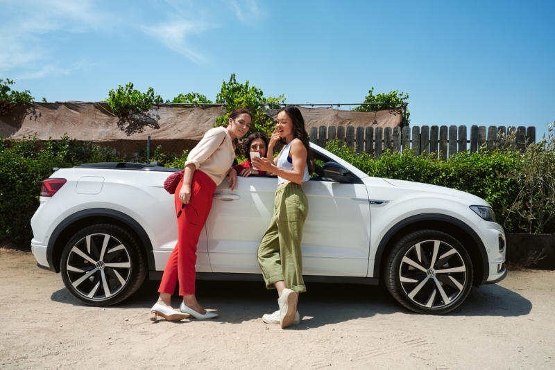 3 amigas hablando y mirando el móvil fuera de un Volkswagen blanco