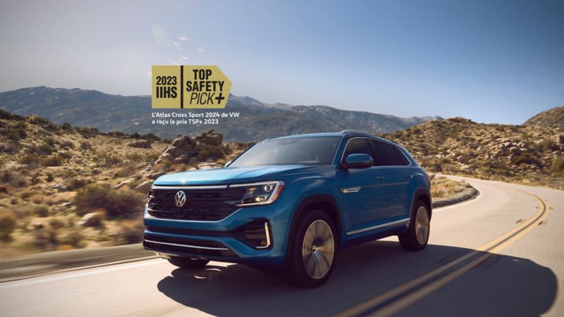 A new, blue 2024 Volkswagen Atlas Cross Sport, driving on the highway.  Superimposed above the vehicle is the award for 2023 IIHS TOP SAFETY PICK+.