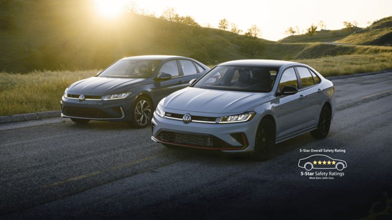 Front view of the blue 2025 Volkswagen Jetta and white Jetta GLi showcasing its new exterior design with scenic hills in the background.