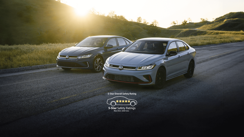 Front view of the blue 2025 Volkswagen Jetta and white Jetta GLi showcasing its new exterior design with scenic hills in the background.