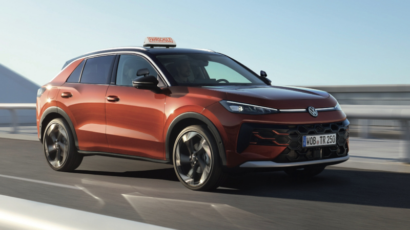 VW T-Roc fährt auf Brücke. Auf dem Dach ist ein ‚Fahrschule‘-Schild