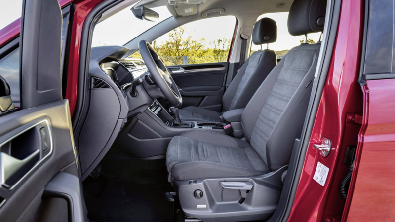 Intérieur d'un Volkswagen Touran rouge avec une vue sur le Cockpit à l'avant par la portière côté conducteur.