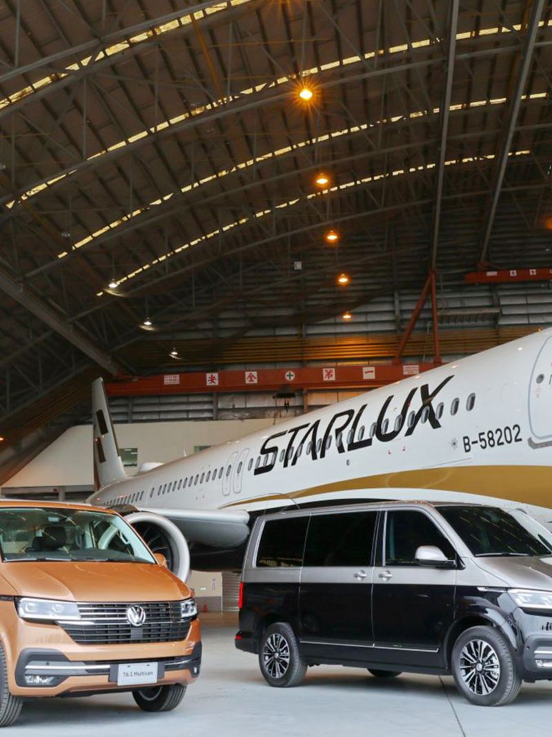 倉庫裡有兩台T6.1 Multivan，一台古銅金色、另一台棕黑雙色，後方有一架飛機