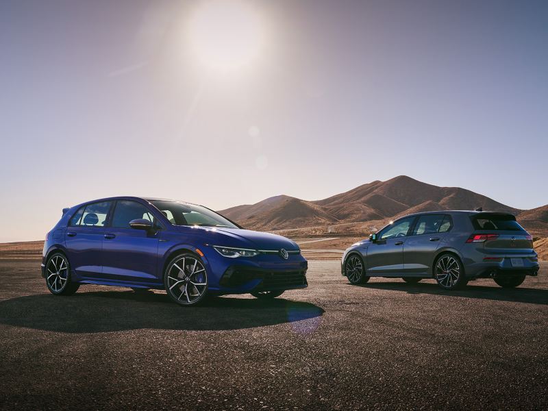 A Golf R and a Golf GTI parked on the road next to the hills.