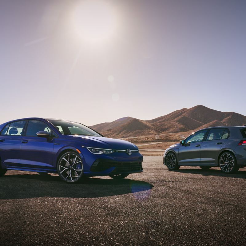 A Golf R and a Golf GTI parked on the road next to the hills.
