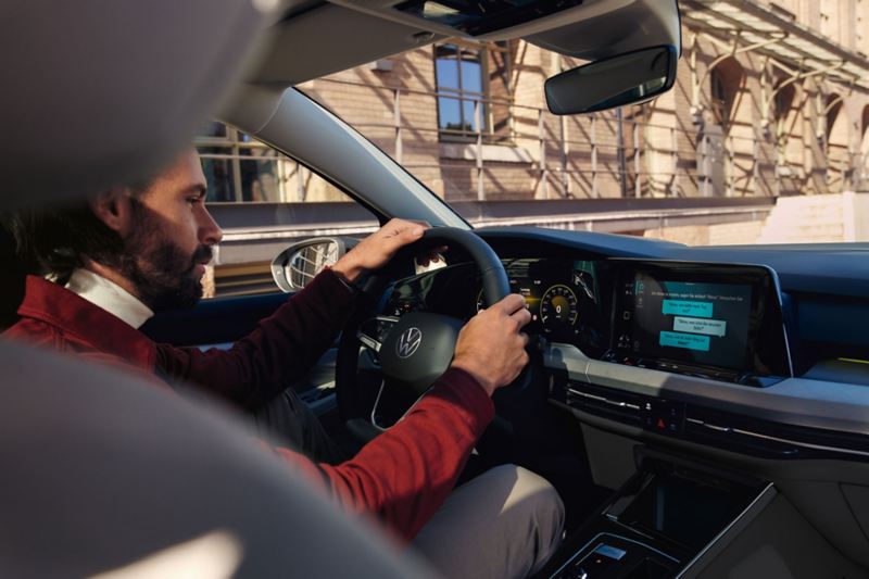 A man at the wheel of a VW Golf using Amazon Alexa as an in-car app.