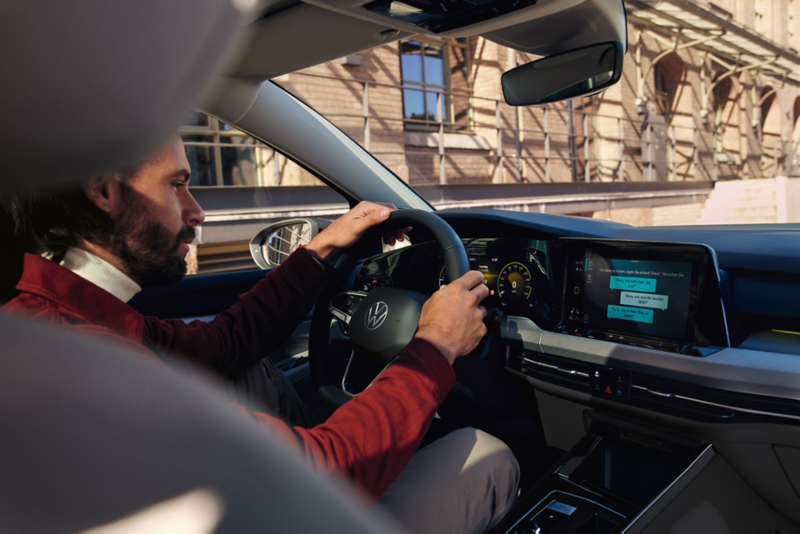 Un homme au volant d'une VW Golf utilisant Amazon Alexa comme application embarquée.