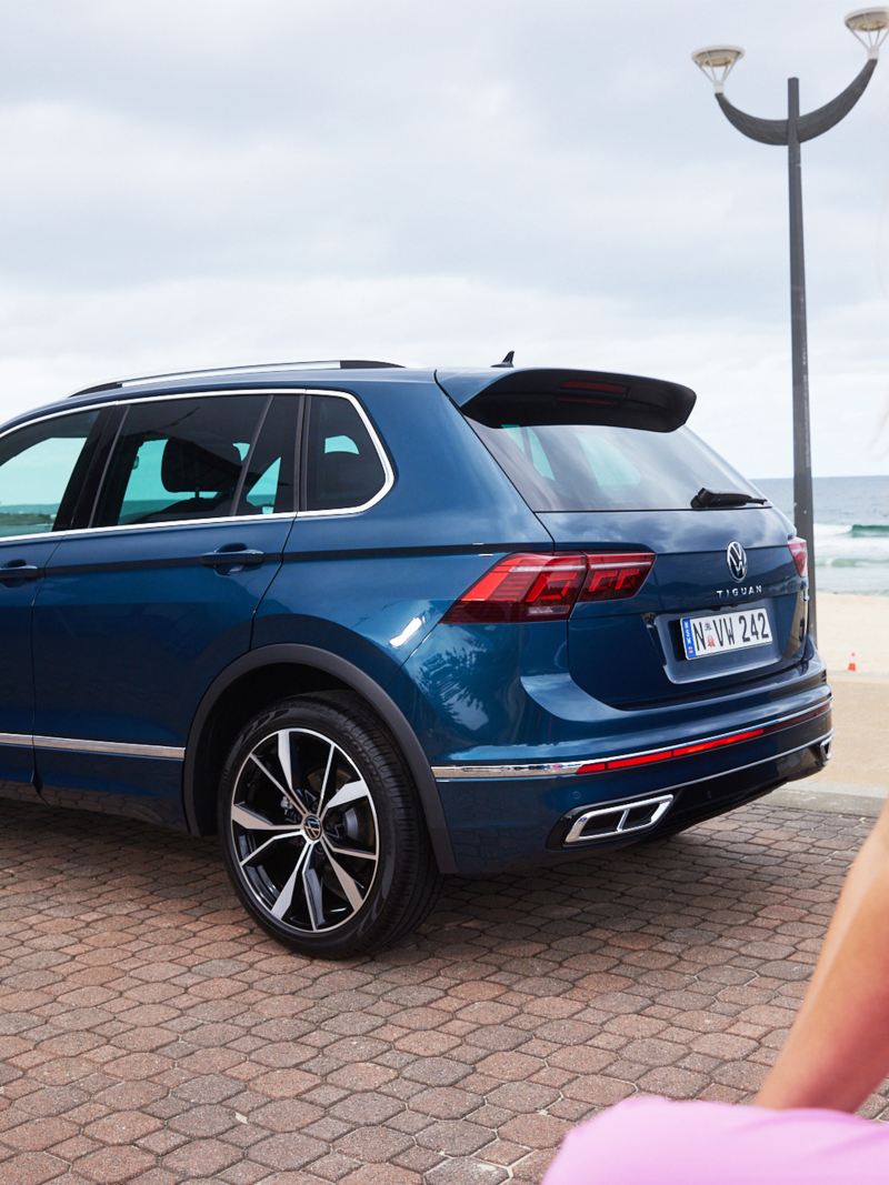 Woman looking backwards with Volkswagen tiguan in background.
