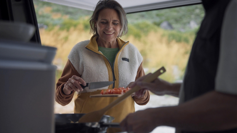 Eine Person steht außerhalb des Californias und gibt geschnittene Tomaten in eine Pfanne.