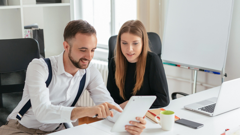 A woman and a man sitting at a desk looking at a document together