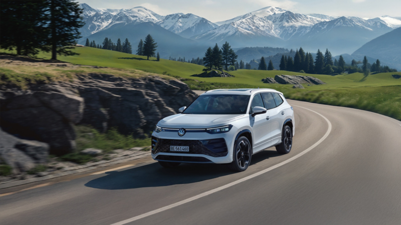 Volkswagen Tayron blanc roule sur une route avec panorama alpin et sommets enneigés.