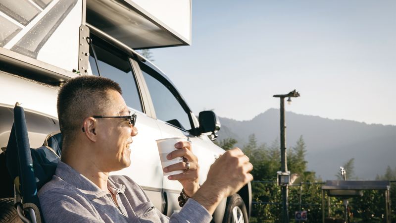 車主康德手拿咖啡享受著露營生活，身後是璀璨銀色的Amarok V6