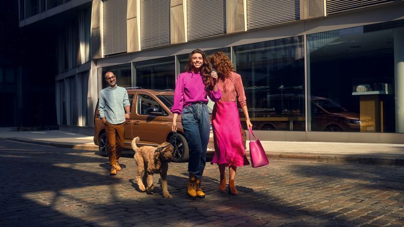 Caddy Maxi情境圖-三個人跟狗站在街上後方有一台古銅金色CaddyMaxi