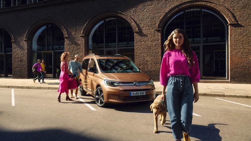 女人跟狗站在街上，後方車主正為女人開古銅金色CaddyMaxi的門
