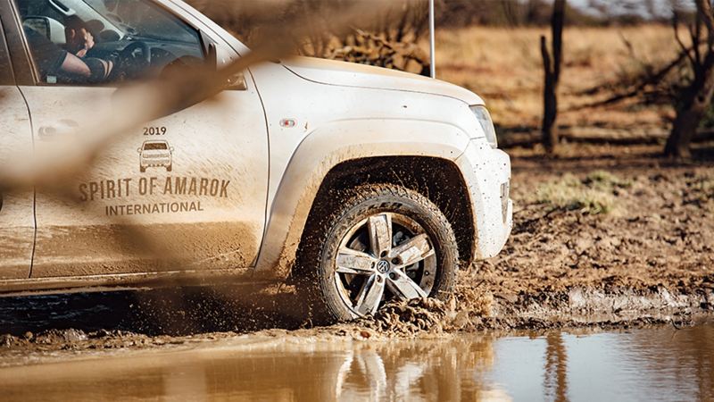 璀璨銀色Amarok 行駛過泥地上的水灘，水花濺起、車側也濺滿泥土痕跡