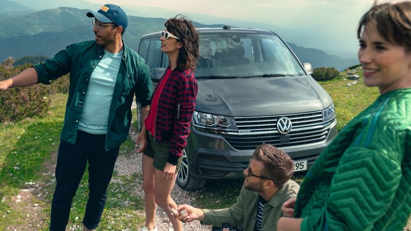 4個視覺年齡30左右的歐美男女開著灰色T6.1 Caravelle出遊，車停在高海拔的草坡上，四人開心在車外欣賞風景