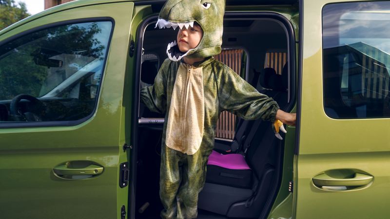 寬敞側滑門，綠色CaddyMaxi打開側滑門，有個小男孩穿恐龍裝站在車門邊