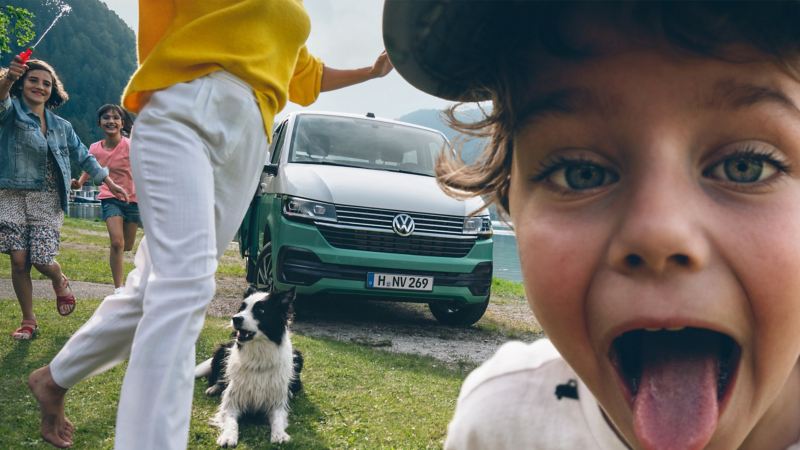 小男孩俏皮地對著鏡頭吐舌頭，而背景是一台月桂葉綠色的Multivan和其他家庭成員正享受著戶外活動