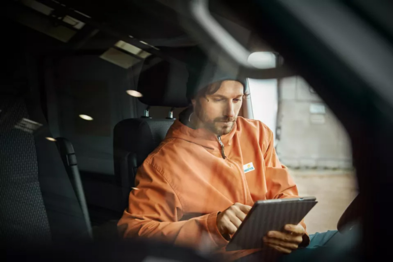 Mężczyzna siedzi za kierownicą dostawczego Volkswagena i robi coś na tablecie.
