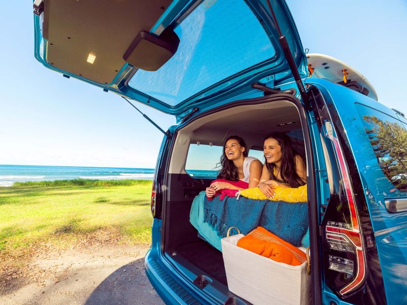 Women laughing in the Volkswagen Caddy California and looking out of the back door. 