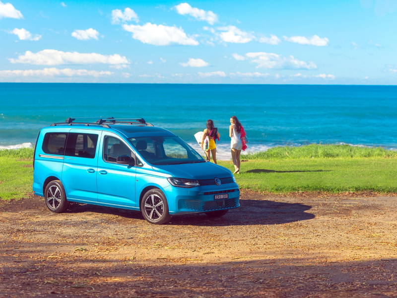 Girls with surfboards at the beach walk away from a Caddy California 