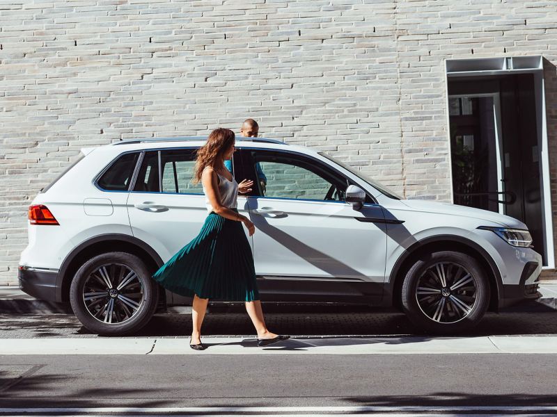 Model in foreground looking down at camera standing next to Volkswagen Tiguan in background.