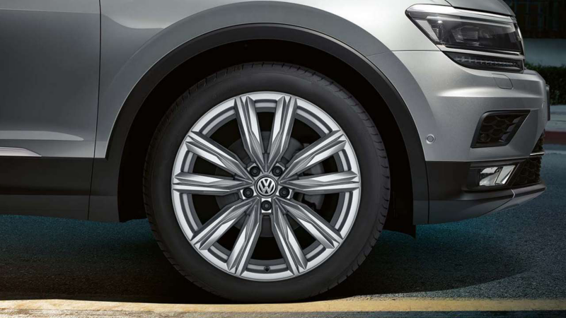 Gros plan sur la roue avant d'une Volkswagen Tiguan grise, montrant la jante en alliage multibranche et une partie du pare-chocs avant.