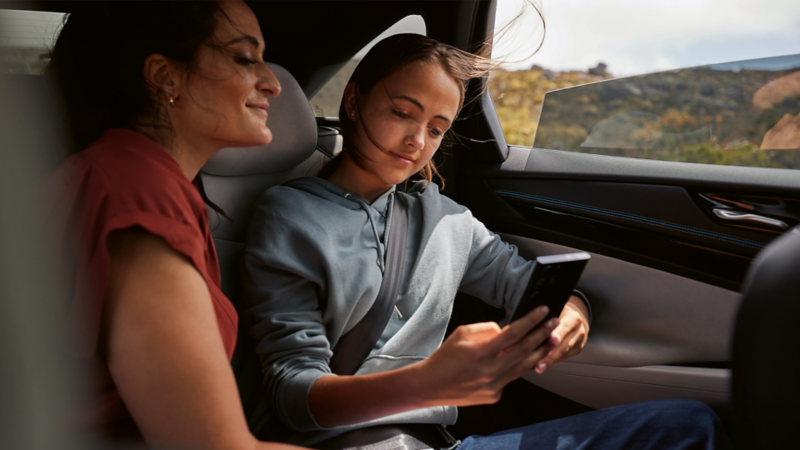 Zwei Personen sitzen auf dem Rücksitz eines Autos, schauen gemeinsam auf ein Smartphone.