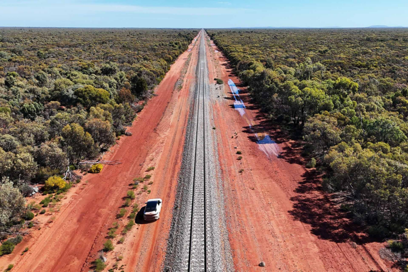 Ariel shot of ID.4 driving through red bushland with forest either side of road