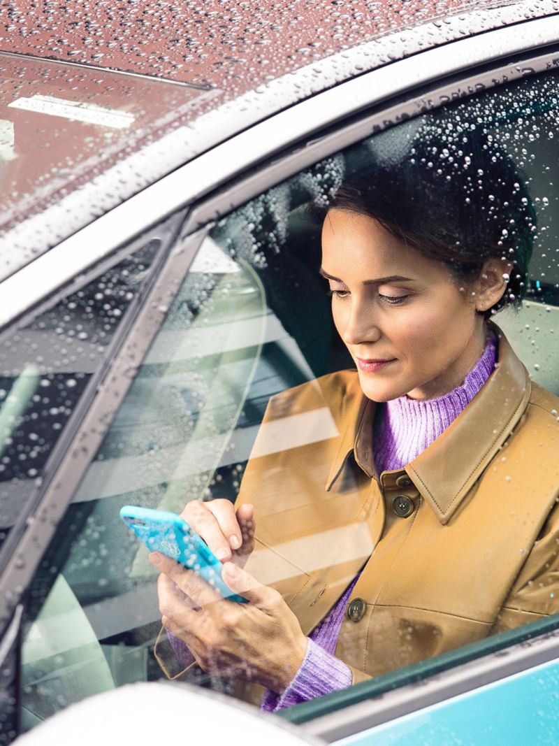 Eine Frau sitzt in ihrem VW ID. mit einem Smartphone in der Hand und bereitet das Over-the-Air Update vor