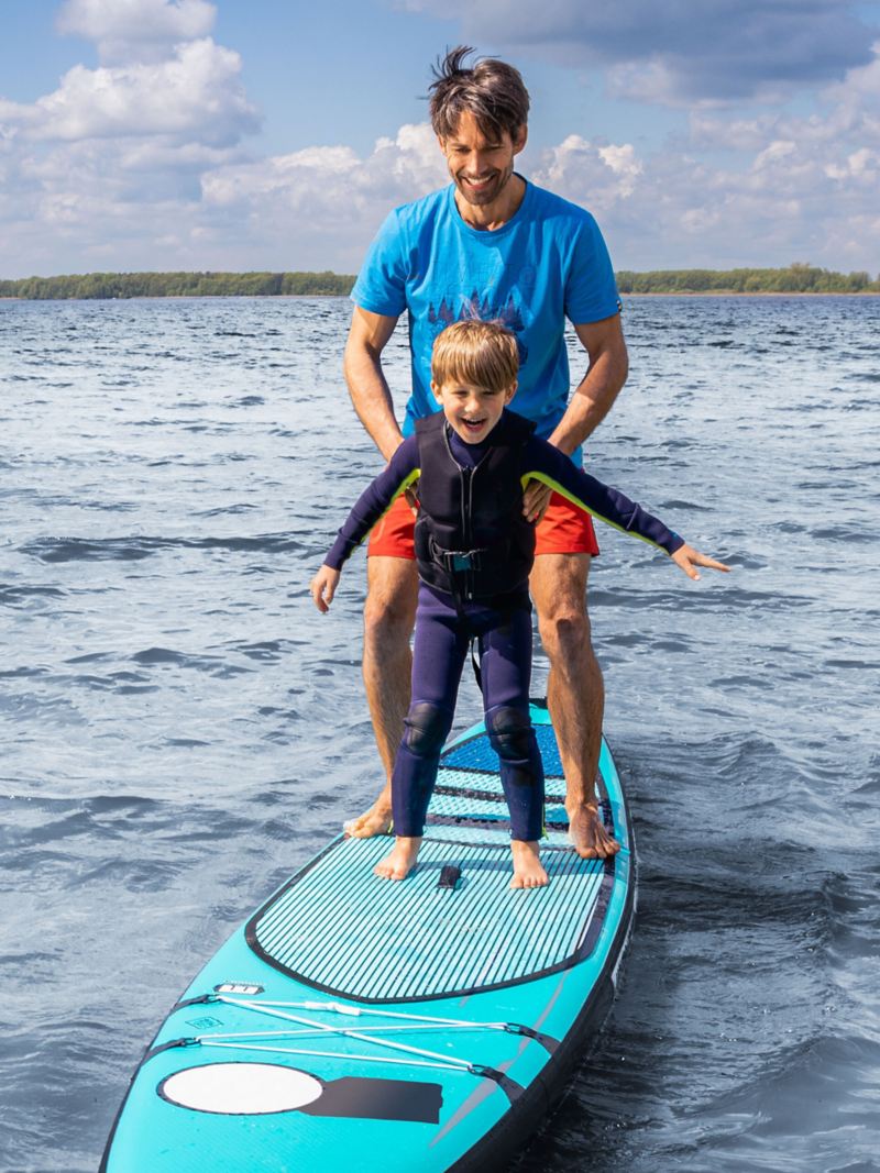 Vater und Sohn stehen auf einem Stand-Up-Paddle Board – Freizeit am See