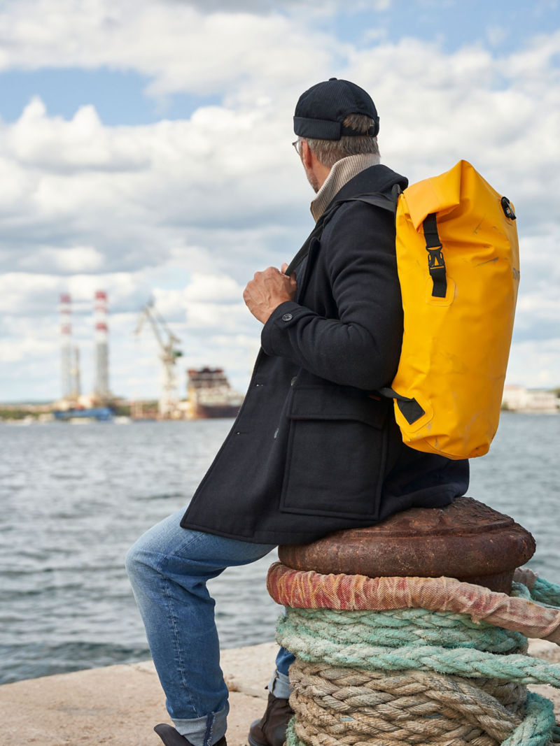 Mann sitzt auf Poller im Hafen und blickt hinaus aufs Meer