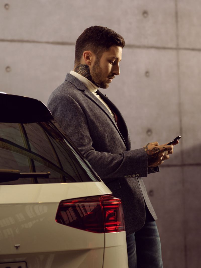 Ein Mann lehnt an seinem VW und ruft die kostenlose Hotline für Unterstützung bei VW Apps und digitalen Diensten an