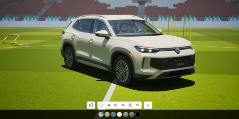 Un élégant VUS Volkswagen Tiguan blanc est présenté sur un terrain de soccer vert vif, entouré de gradins de stade et d'équipements d'entraînement. Le véhicule est positionné en angle, mettant en valeur son design moderne et sa calandre audacieuse.