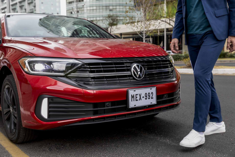 Cofre de seminuevo Jetta color rojo con hombre que camina frente al auto de Volkswagen. 