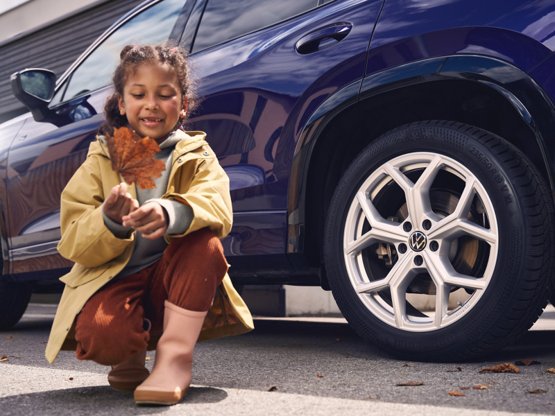 Mädchen hockt vor blauem VW Tayron, im Fokus die Räder