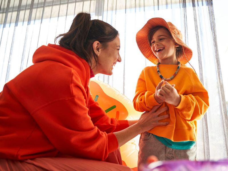 Eine Frau und ein Kind in roter und oranger Kleidung lachen zusammen