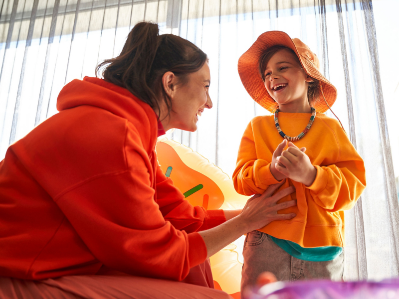 Frau und Kind in roter und oranger Kleidung lachen zusammen