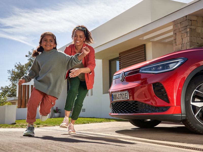 Mutter und Tochter spielen Fangen neben einem parkenden roten VW ID.5