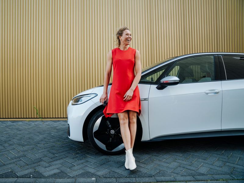 Eine lachende Frau lehnt an ihrem VW E-Auto – nachhaltige Elektromobilität