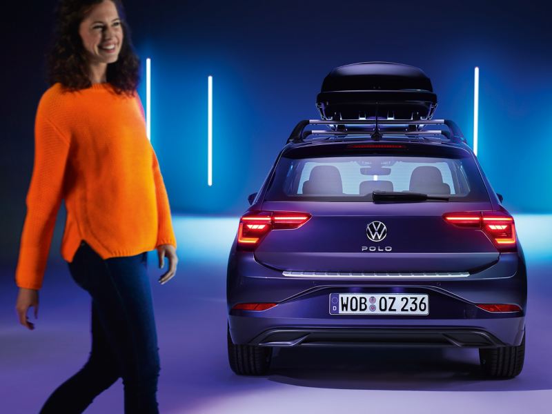 Volkswagen Polo con un portaequipaje visto desde atrás y una chica de naranja