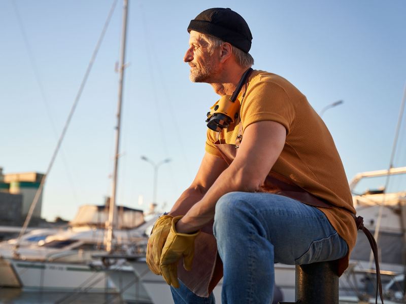 Ein Mann sitzt im Hafen bei den Booten und schaut verträumt aufs Meer