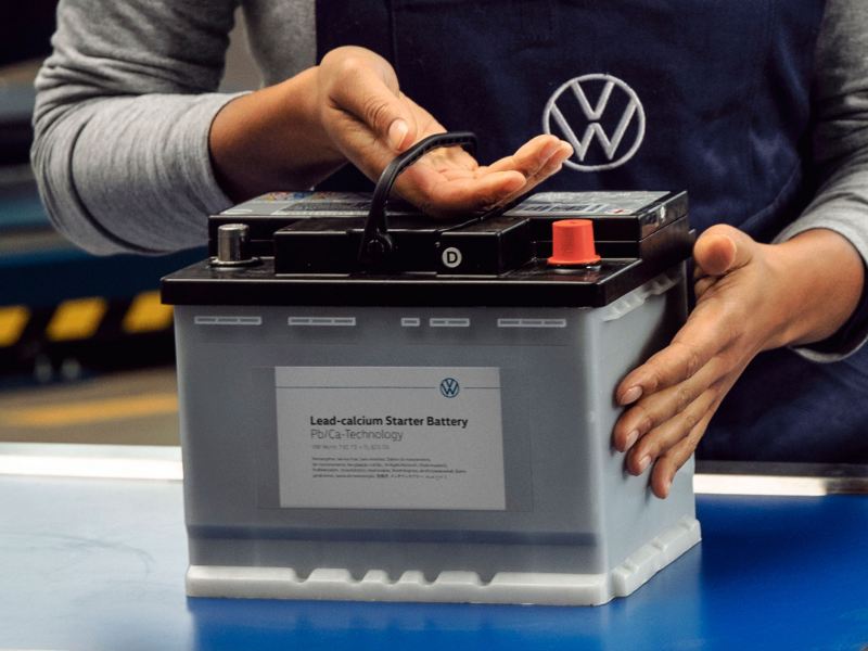 En VW-servicemedarbeider holder et Volkswagen-batteri – resirkulering av batterier