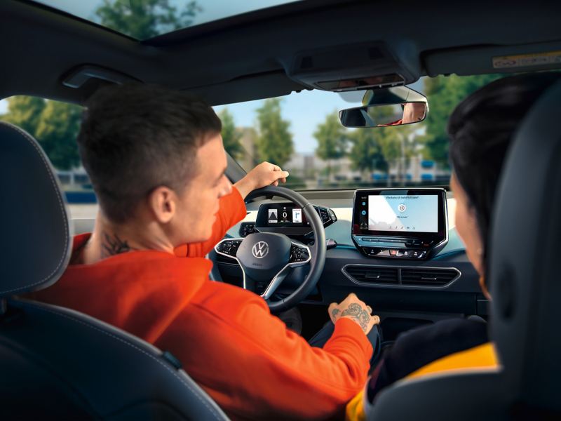 Un uomo, seduto al posto di guida della sua ID. Volkswagen, utilizza il sistema di infotainment e attraverso il display touch.