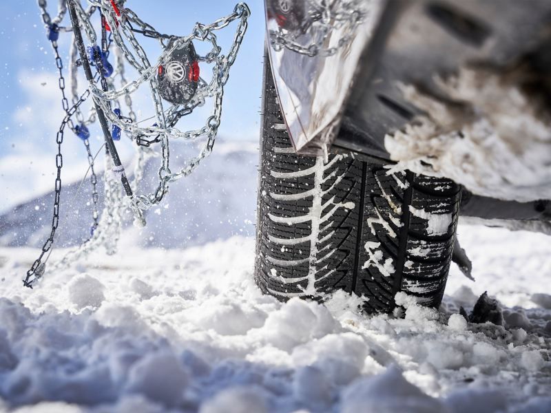 Detailaufnahme von Schneeketten neben dem Reifen eines VW Autos im Schnee