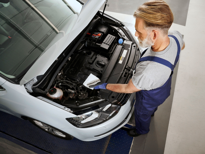 Top view of a VW Sharan 2 with open bonnet, VW service employee measures the oil level