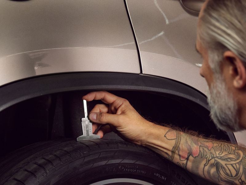 Un empleado del servicio técnico mide la profundidad de la banda de rodadura de los neumáticos