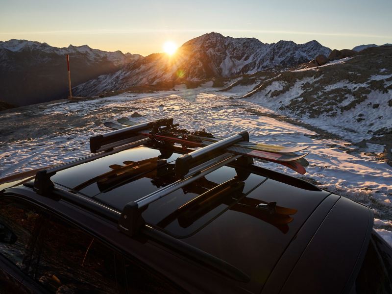 Ein VW Auto mit Transportlösungen von Volkswagen Zubehör vor einer verschneiten Berglandschaft mit Sonnenuntergang