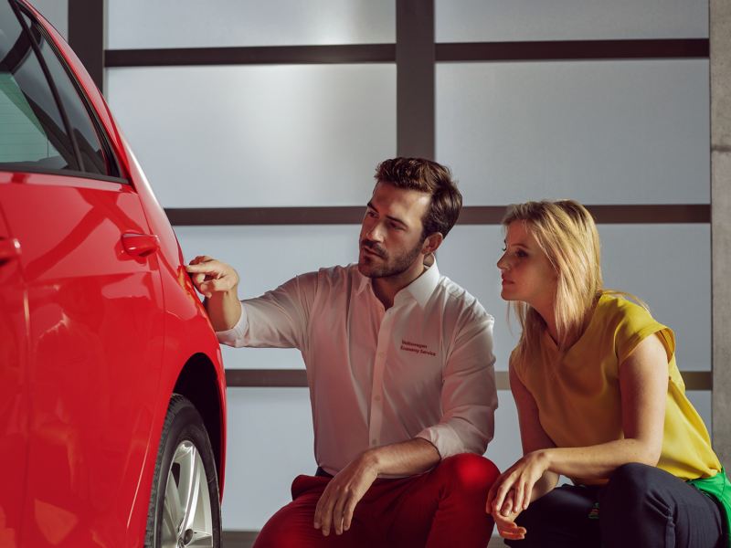 Ein Servicemitarbeiter vom Volkswagen Economy Service zeigt einer Kundin etwas an einem roten VW Auto