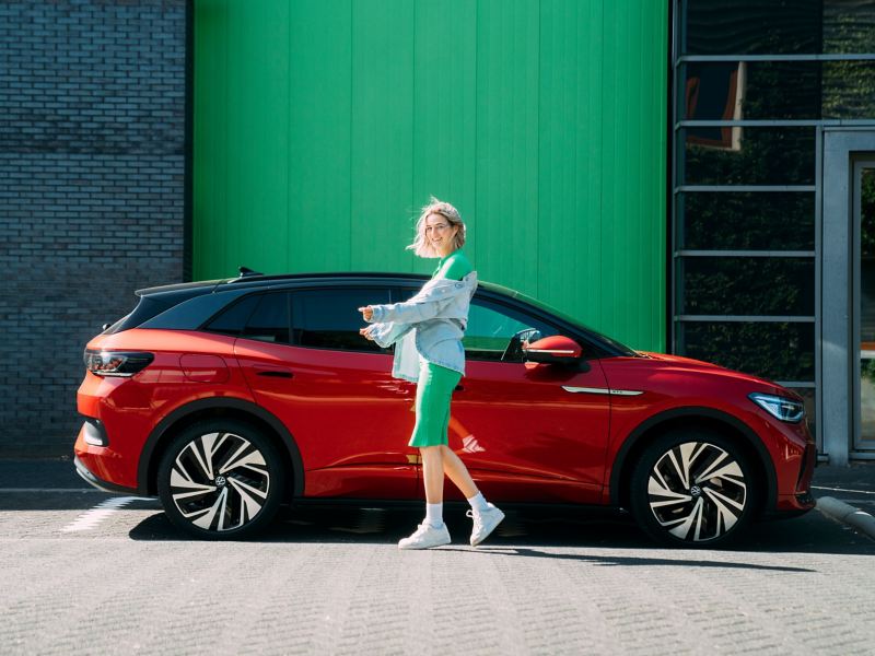 Eine Frau steht vor ihrem parkenden VW ID. Modell in Rot